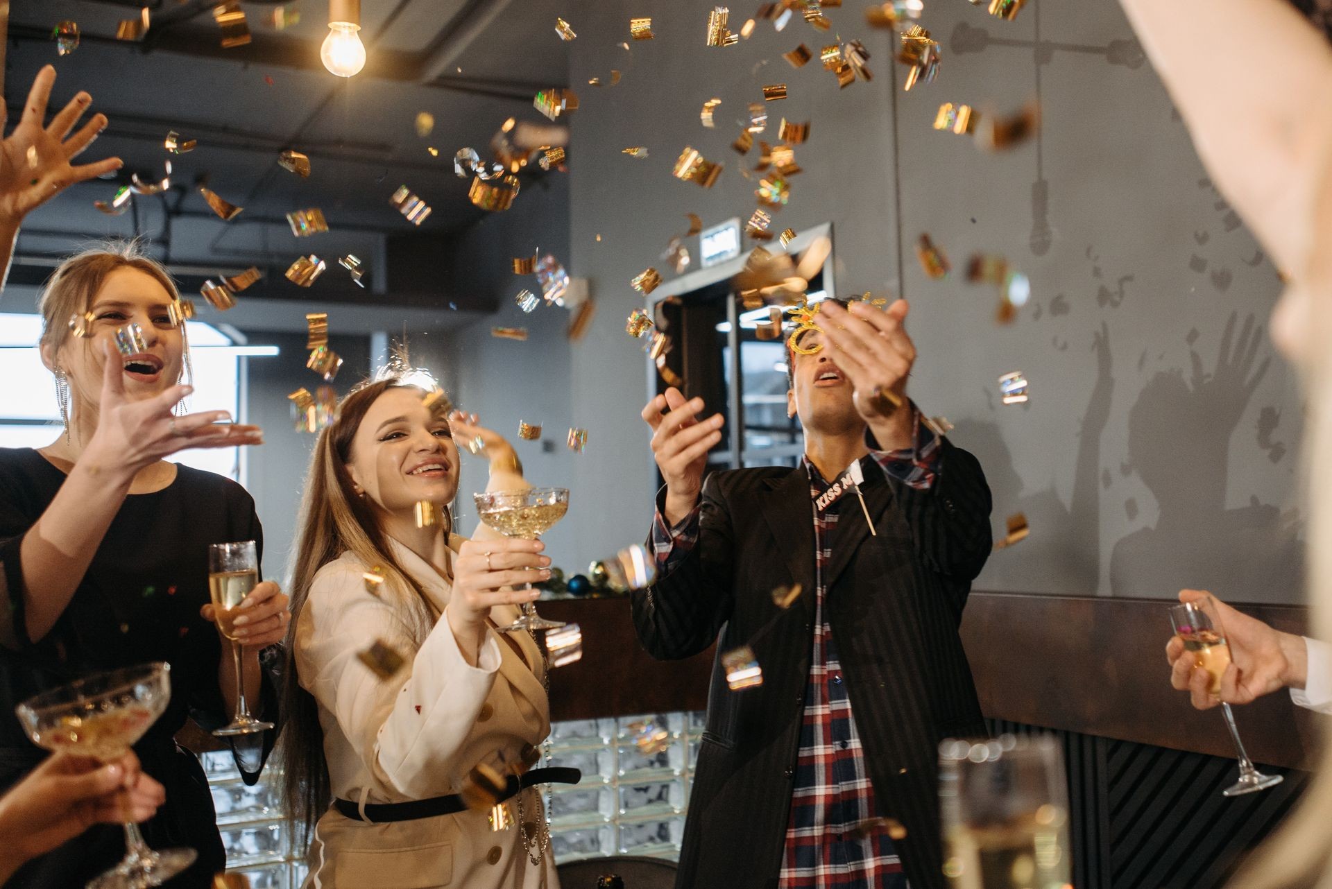 Group of people celebrating with champagne glasses and throwing confetti in a festive indoor setting.