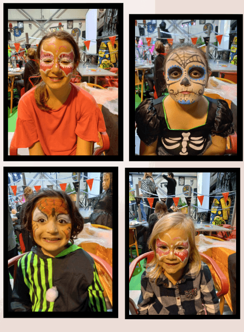 Four children with painted faces in a festive indoor setting.