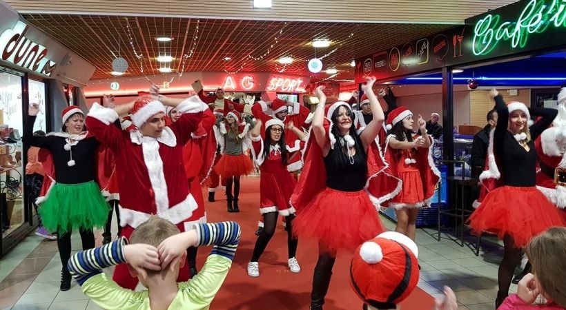 Group of people dressed in festive holiday costumes performing a dance in a decorated indoor space.