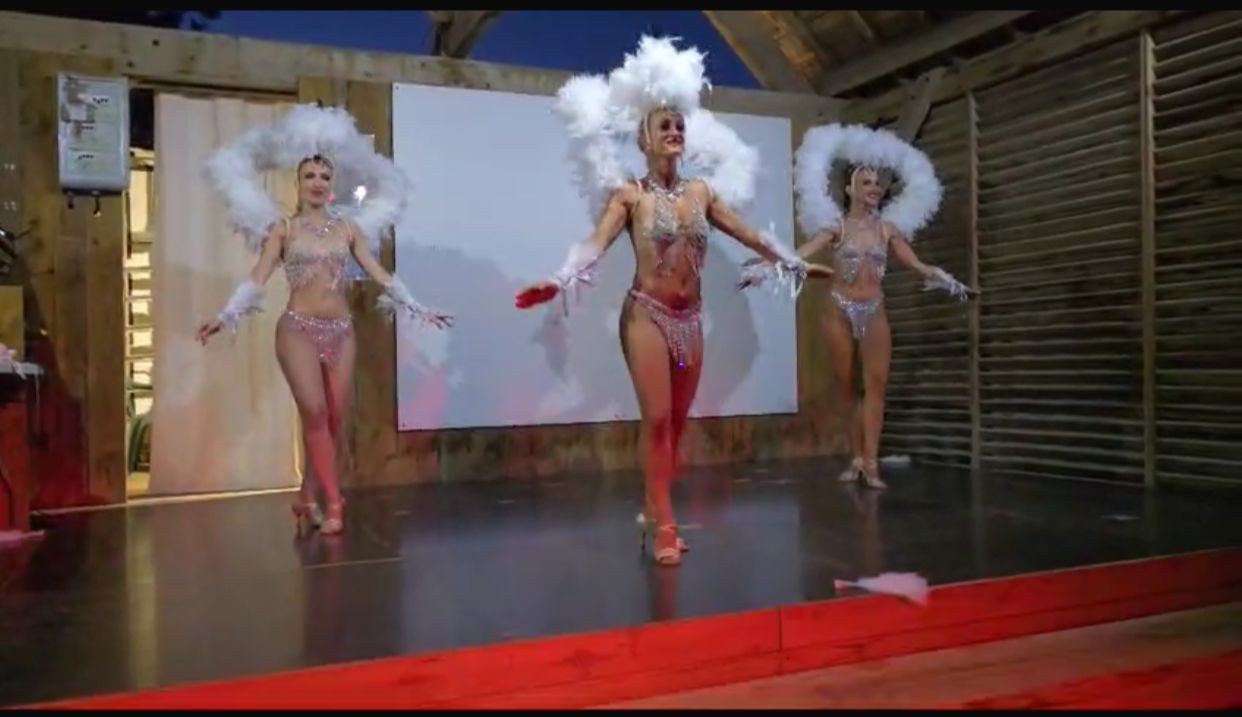 Three dancers in sparkling outfits with feathered headdresses performing on stage.