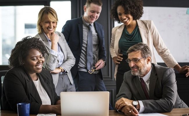 Group of business people smiling and looking at a laptop screen during an office meeting.