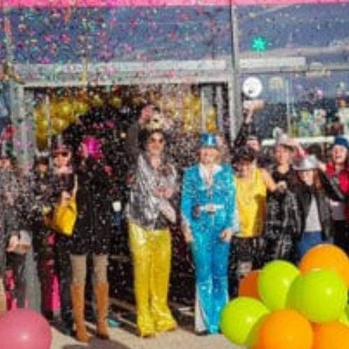 Group of people in colorful outfits celebrating outside a building with confetti and balloons.