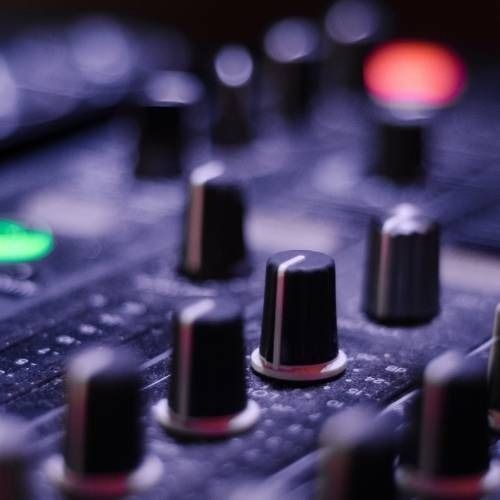 Close-up view of audio mixer controls, featuring knobs and buttons with glowing lights in the background.